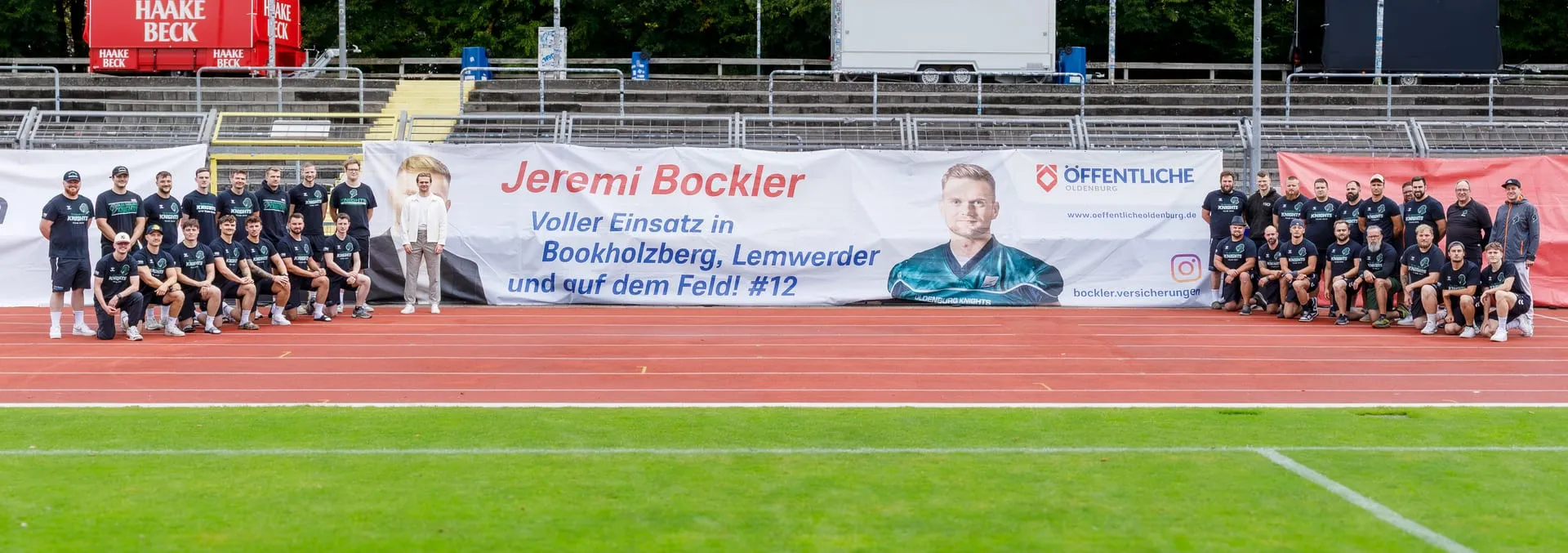 Das Team der Oldenburg Knights vor dem Sponsoring-Banner von Jeremi Bockler im Stadion
